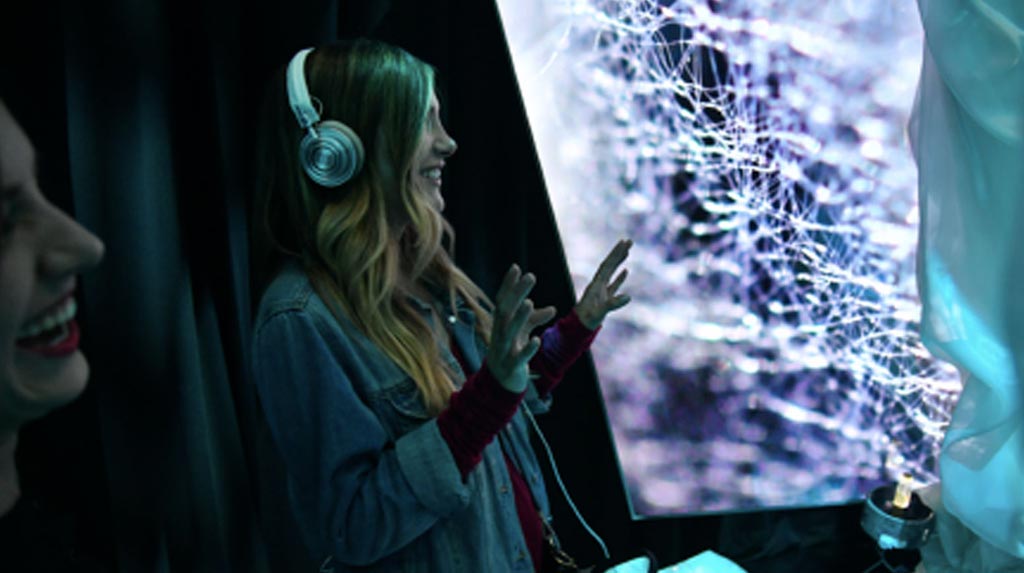 Girl standing in front of installation with headphones on.